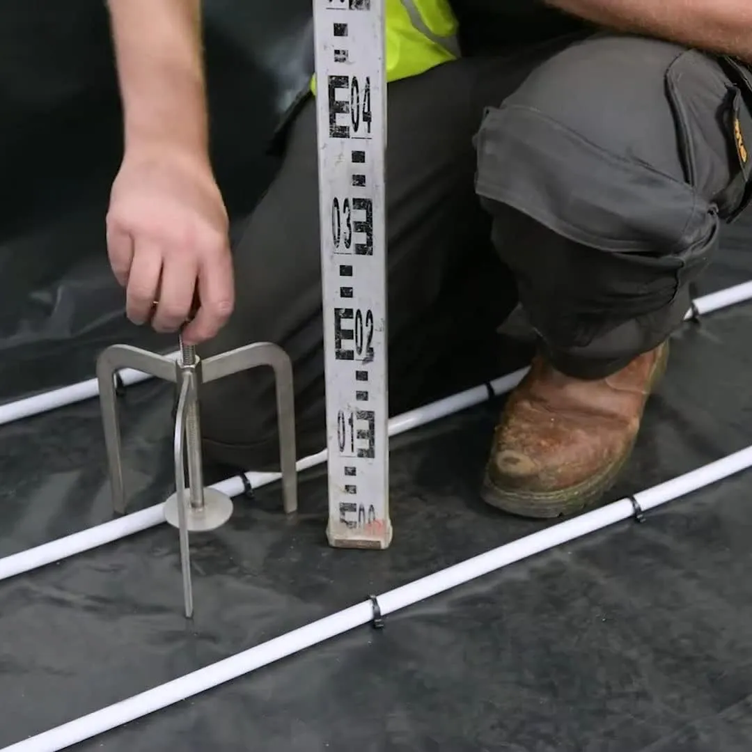 Worker squatting over UFH pipes adjusting the level of a Metex screed tripod